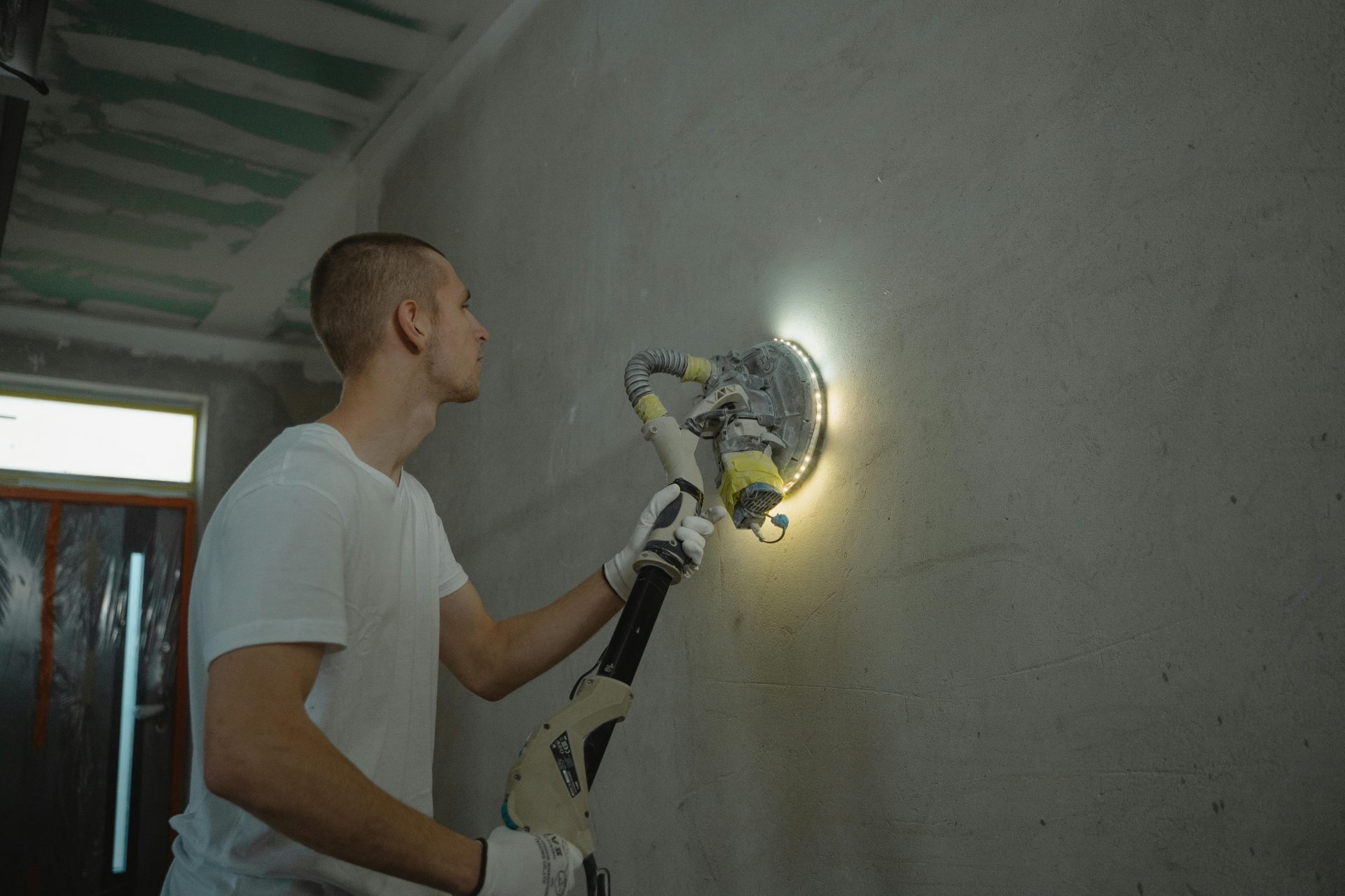 Foto eines Mannes, der bei einem Renovierungsprojekt im Innenbereich eines Hauses mit einem Elektrowerkzeug eine Wand schleift.