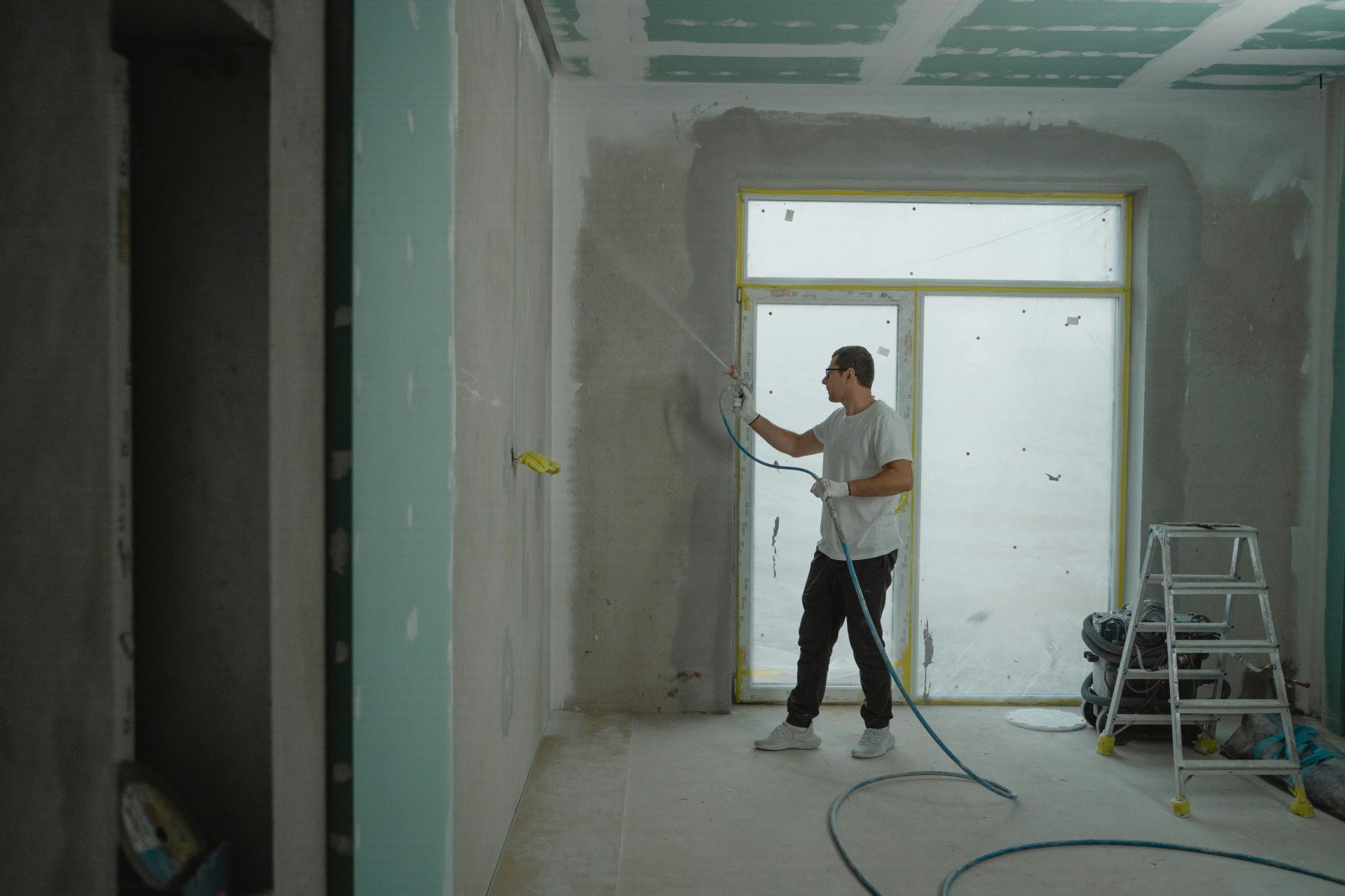 Ein Mann sprüht Farbe auf eine Wand, während er mit professioneller Ausrüstung einen Innenraum renoviert.